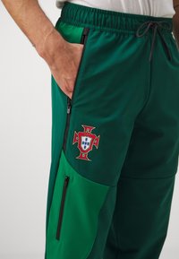 Gröna sportbyxor med en framträdande broderad Portugal-vapensköld. Inkluderar fickor med dragkedja och en elastisk midja.