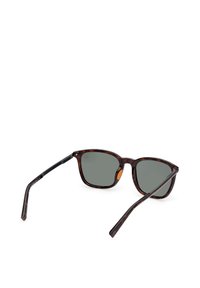 Lunettes de soleil à monture carrée en écaille avec verres gris foncé, branches fines noires et petit détail orange à l'intérieur d'un verre.