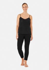 Zwart topje met kantafwerking en dunne bandjes, gecombineerd met zwarte aansluitende leggings. Zachte stof, gladde textuur, minimalistisch ontwerp.