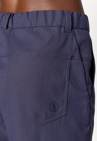 Marineblaue Shorts mit glatter Textur, elastischem Bund und einer Gesäßtasche mit einem runden Logo. Sichtbare Ziernähte sind vorhanden.