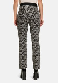 Eng anliegende schwarze Hose mit einem weißen und beigen Leopardenmuster, ausgestattet mit einem breiten elastischen Bund und geradem Bein. Glänzende schwarze High Heels.
