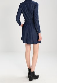 Jeanskjol i mörkblått, med långa ärmar, midjebälte och utsvängd kjol. Matchad med svarta ankelboots.