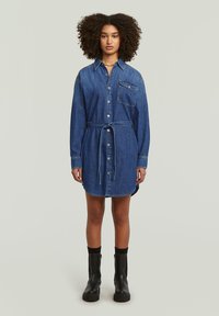 Φόρεμα από τζιν, μακριά μανίκια, κουμπιά μπροστά, τσέπη στο στήθος, μέση με ζώνη, ευθεία γραμμή, μπλε χρώμα, συνδυασμένο με μαύρες μπότες με περιστερωτή σόλα.