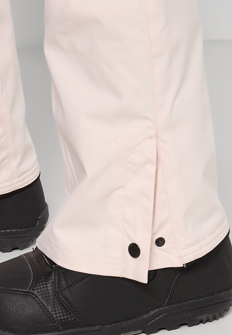 Jasnoróżowe wodoodporne spodnie o prostym kroju z zatrzaskiem na dole, w połączeniu z czarnymi ocieplanymi zimowymi butami.