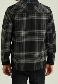 Černá a šedá kockovaná flanelová košile s dlouhými rukávy, knoflíkovými manžetami a detailem na yoke vzadu, vyrobená z měkké, texturované látky.