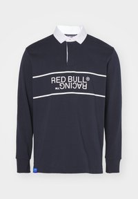 Námořnická polo košile s dlouhým rukávem, bílým límcem, červenobílým grafickým logem "RED BULL RACING" na přední straně a modrým akcentem na lemu.