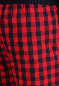 Tela a cuadros en rojo y marino con una textura suave, que presenta una cintura elástica y un bolsillo trasero para almacenamiento.