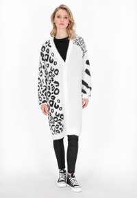 Cardigan lungo bianco e nero con motivi leopardati e a righe, realizzato in materiale morbido e peloso, con scollatura a V e design aperto.
