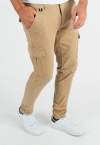 Pantalons cargo kaki au design ajusté, avec poches latérales et un tissu texturé. Associés à des baskets blanches avec des accents noirs.