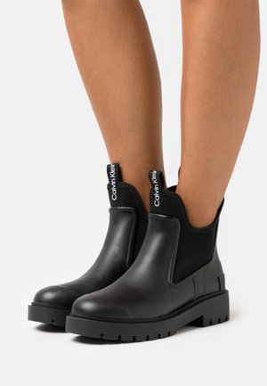 Botas de tobillo negras hechas con cuero suave y paneles laterales elásticos. Presentan una suela de goma gruesa y pestañas decorativas.