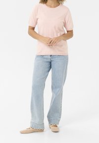 Jasnoróżowy sweter z krótkim rękawem w textured kropki, zestawiony z jasnoniebieskimi spodniami typu high-waisted oraz beżowymi, plecionymi butami wsuwanymi.