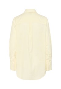 Camicia giallo chiaro con colletto a bottone, maniche lunghe e una sottile trama testurizzata. La piega posteriore aggiunge forma e dettaglio.