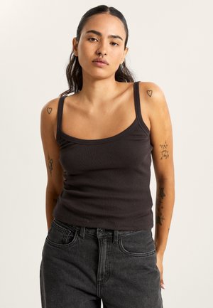 Schwarzes, enganliegendes Tanktop mit dünnen Trägern, aus elastischem Stoff gefertigt. Kombiniert mit hochgeschnittenen schwarzen Jeans, die eine glatte Textur zeigen.