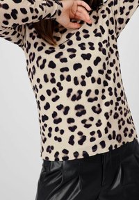 Beige ja musta leopardiampumismalli, millel on pikad varrukad, V-kaelus ja pehme, sile tekstuur. Kandub mustade volangpükstega.