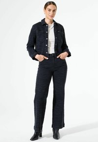 Veste en denim bleu foncé et pantalon assorti avec un motif zèbre subtil. L'ensemble comporte un col de chemise et des fermetures à boutons. Bottines noires.