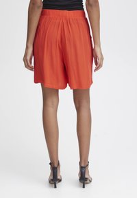 Rode shorts gemaakt van een lichtgewicht materiaal, met een relaxte pasvorm, plooien en een elastische tailleband. Gemaakt met zwarte hakken.
