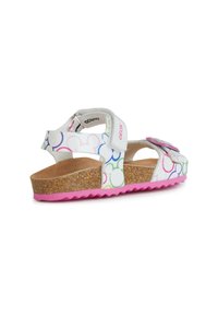 Sandalia blanca con patrones circulares temáticos de Disney en colores, suela de corcho, parte inferior de goma rosa y correa ajustable con hebilla.