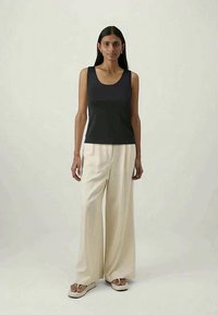 Top senza maniche di colore blu navy con scollatura rotonda, abbinato a pantaloni larghi color crema e infradito. Tessuto liscio, design semplice, accenti minimal.