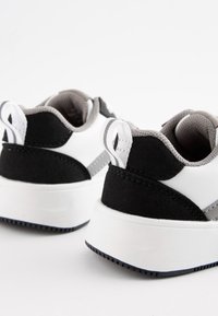Zapatillas en blanco y negro con un upper de tejido texturizado, cuello acolchado y una suela de goma blanca con un patrón de agarre texturizado.