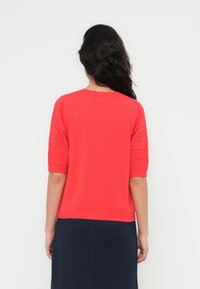 Πουλόβερ πλεκτό σε κοραλλί απόχρωση με κοντά, υφασμένα μανίκια και στρογγυλή λαιμόκοψη. Ομαλό ύφασμα στο σώμα και ριμπ λεπτομέρειες στα μανίκια και τη μέση.