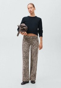 Pullover nero in maglia abbinato a pantaloni a gamba larga con stampa leopardata marrone. La modella tiene una borsa marrone ed indossa scarpe nere con borchie.