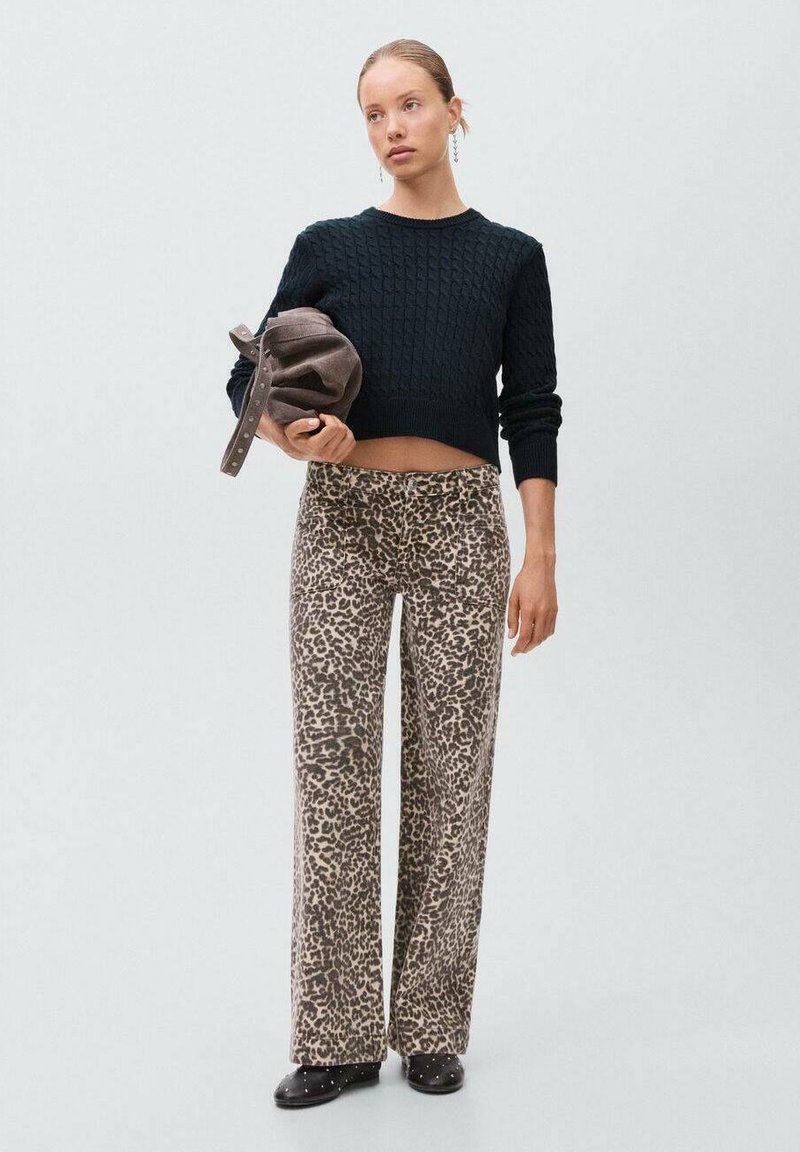Pullover nero in maglia abbinato a pantaloni a gamba larga con stampa leopardata marrone. La modella tiene una borsa marrone ed indossa scarpe nere con borchie.