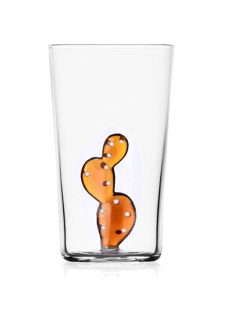 Przezroczysta, pusta szklanka z bursztynowym, kaktusopodobnym obiektem z białymi kropkami w środku, umieszczona na białym tle.