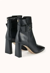 Bottines en cuir noir à bout pointu, avec un talon bloc et des accents de boucle au niveau de la cheville, présentant une texture lisse et des détails en métal doré.