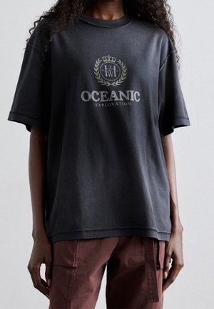 Svart oversized t-shirt i mjuk bomull. Har ett grafiskt tryck med "OCEANIC EXPLORATION" och ett dekorativt krondesign. Kortsärmad.