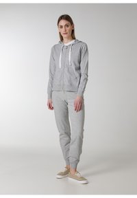 Grå zip-up hoodie och matchande joggers i mjukt tyg, med vita dragskor, sidofickor och ribbade muddar vid anklarna.
