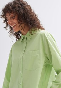 Light green button-up shirt made of soft fabric, featuring a pocket on the left, pointed collar, and slightly loose-fitting sleeves.