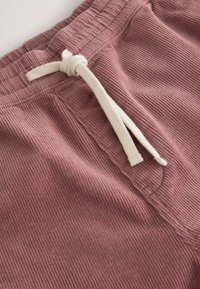 Gros plan sur un pantalon en velours côtelé rose poussiéreux avec une taille élastique et un cordon blanc noué.