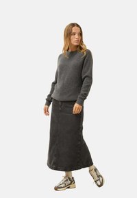 Harmaa neule, jossa on teksturoitu neulonta, yhdistetty pitkän mustan farkuhameen kanssa. Täydennetty kuvioiduilla lenkkareilla ja nilkkasukilla.