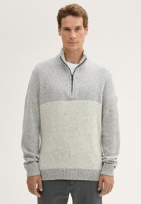 Grijze zip-up trui met een twee-tint ontwerp, bestaande uit een lichtgrijze bovenhelft en een textuur onderhelft, met ribbels aan de mouwen en onderkant.