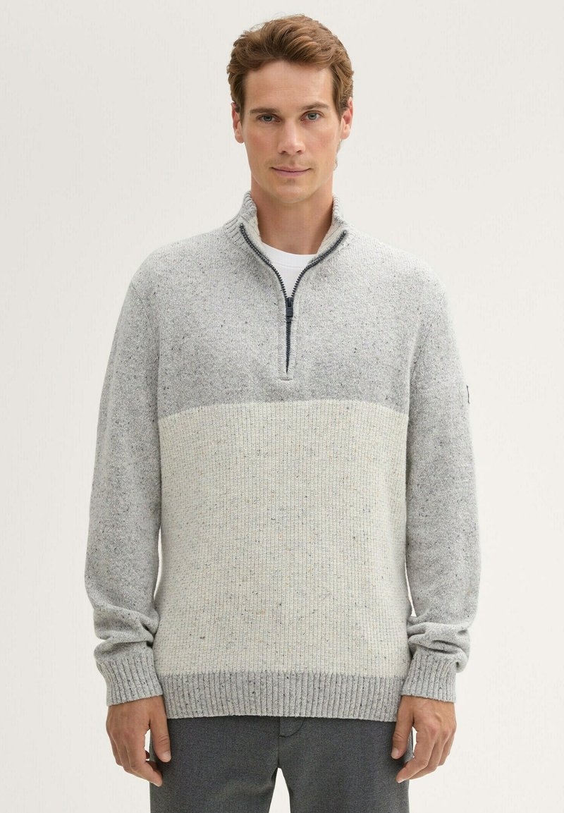 Grijze zip-up trui met een twee-tint ontwerp, bestaande uit een lichtgrijze bovenhelft en een textuur onderhelft, met ribbels aan de mouwen en onderkant.