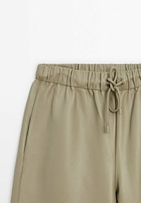 Pantalon beige en faux cuir avec taille élastique et lien à nouer à l'avant, présenté sur fond blanc.