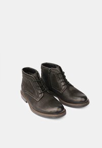 Botas de tobillo de cuero negro con detalles de costura, cierre de cordones, cremallera lateral, punta redonda y suela marrón en contraste.