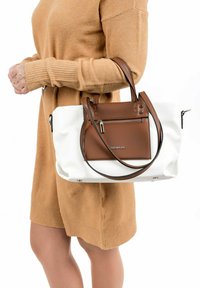 Borsa tote in pelle con parte superiore marrone e corpo bianco, manici marroni e tasca con zip frontale. Tessuto liscio con accenti argento.