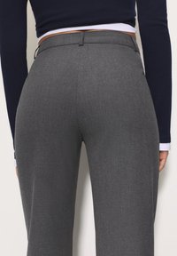 Grijze op maat gemaakte broek met een gladde textuur, voorzien van een taille met middelhoog model en achterzakken, aangevuld met een subtiel stofpatroon.