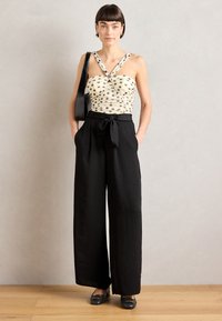 Pantaloni neri a gamba larga con cintura legata, abbinati a un top crema con pois neri e spalline incrociate. Scarpe nere completano il look.