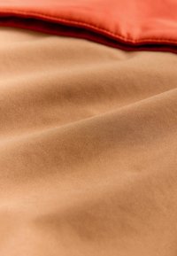 Un material maro cu o textură netedă, suprapus cu un material portocaliu la marginea superioară. Materialul portocaliu are un luciu subtil.