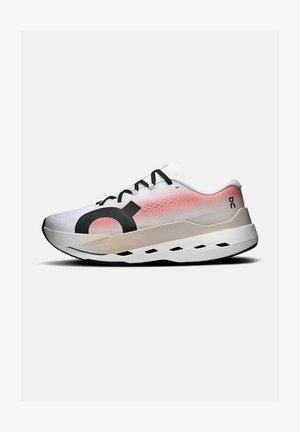 Zapatilla de correr blanca y rosa con cordones negros, suela gruesa con detalles negros y gran logotipo negro en el lateral sobre un fondo gris.