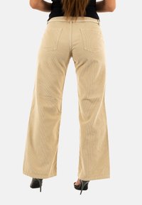 Beige corduroy wijde broek met een gestructureerde oppervlakte, voorzien van achterzakken en een middellange taille. Gestyled met zwarte hoge hakken.