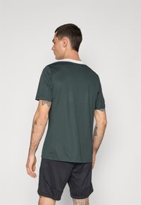 M�ørkegrøn kortærmet T-shirt med hvid krave. Lavet af struktureret stof, med en afslappet pasform og synlige tatoveringer på armen.