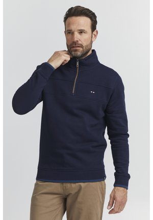 Marineblaues Viertelreißverschluss-Pullover mit gerippten Bündchen und Saum, ausgestattet mit einem kleinen Logo und kontrastierenden Reißverschlussdetails. Weiche, glatte Textur.