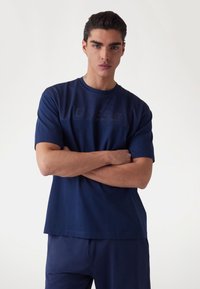 Námořnická modrá sportovní tričko vyrobené z prodyšné síťoviny, s texturovanou panelem na hrudi a krátkými rukávy.