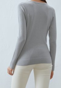 Maglione grigio a maniche lunghe in un fine tessuto a maglia, con scollatura a barchetta e una forma aderente, abbinato a pantaloni chiari.
