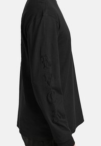Zwarte lange mouwen shirt van katoen, met geborduurde letters "RVC" langs de linkermouw. Eenvoudig ontwerp, ronde halslijn en relaxed fit.