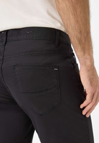 Zwarte spijkerbroek van stof met een rechte snit, zichtbare stiksels, een logopatch op de tailleband en een achterzak met een subtiel logodetail.