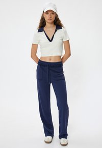 Witte cropped polo met een marineblauwe kraag, gecombineerd met marineblauwe sweatpants met een trekkoord en zijzakken, aangevuld met witte sneakers.